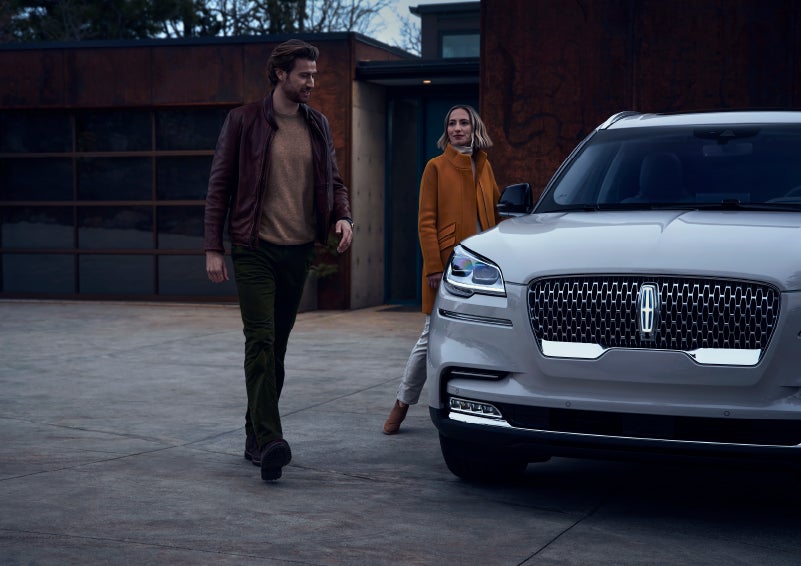 A man and a woman approaching a 2024 Lincoln Aviator® SUV, which illuminates certain lights when they are close | Crossroads Lincoln of Southern Pines in Southern Pines NC